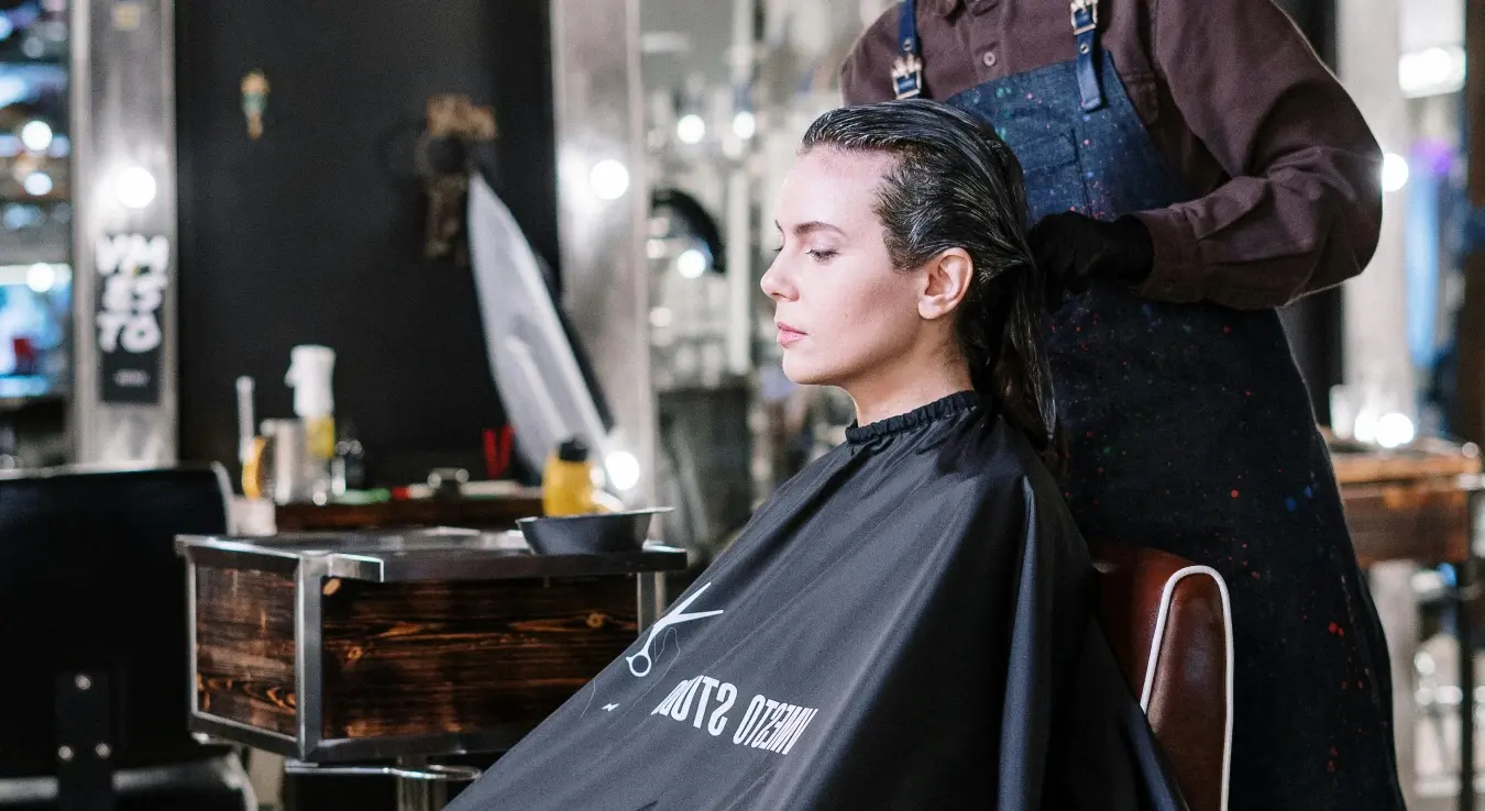 Млада трудница сједи у фризерском салону док јој фризер обавља фарбање косе у трудноћи.