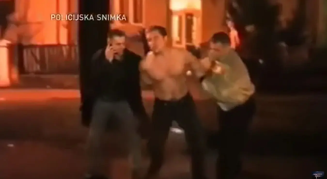 Привођење Срђана Млађана након убиства полицајца. Без мајице са лисицама воде га два полицајца у цивилу