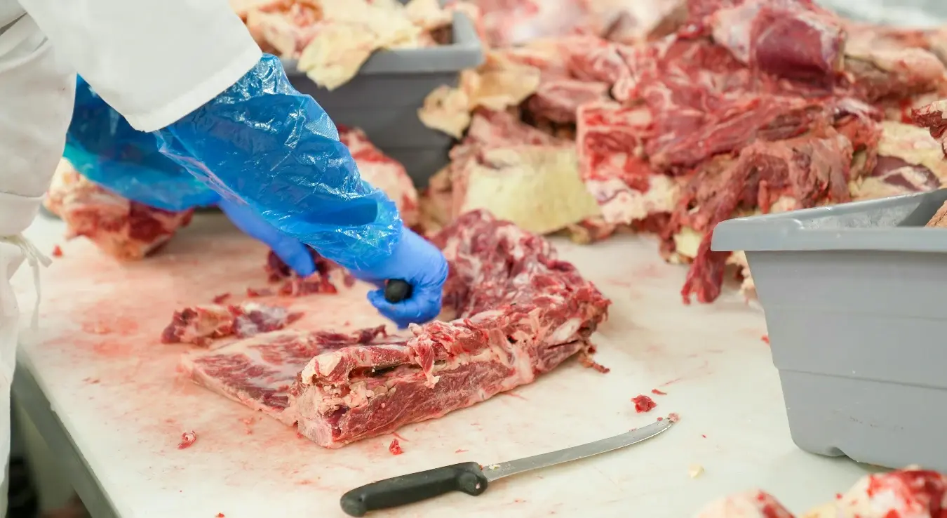 Месар сијече месо на дасци, док носи рукавице.