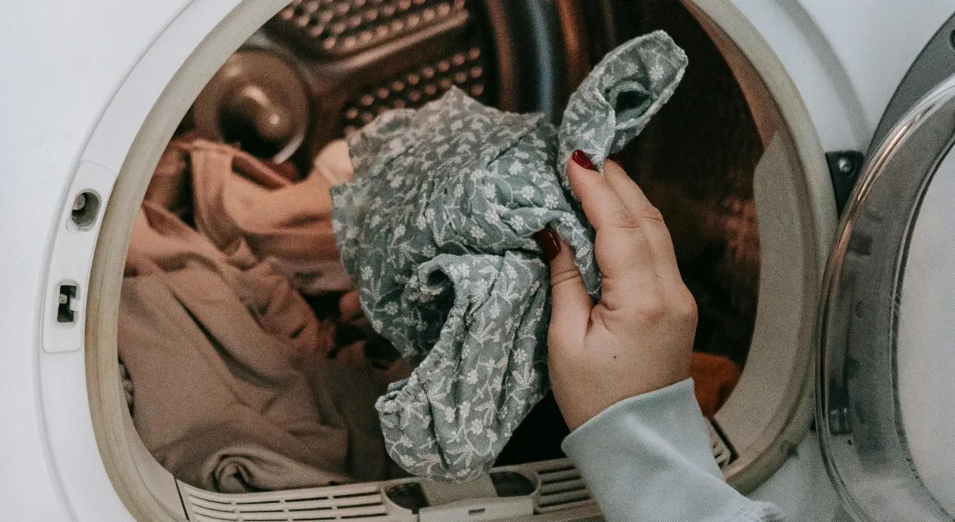 Жена руком извлачи веш из машине за сушење веша.