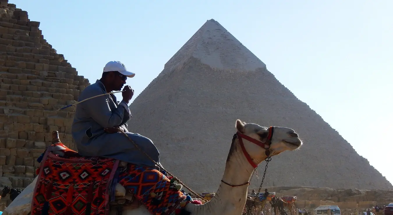 Мушкарац јаше камилу док пролази поред пирамида.