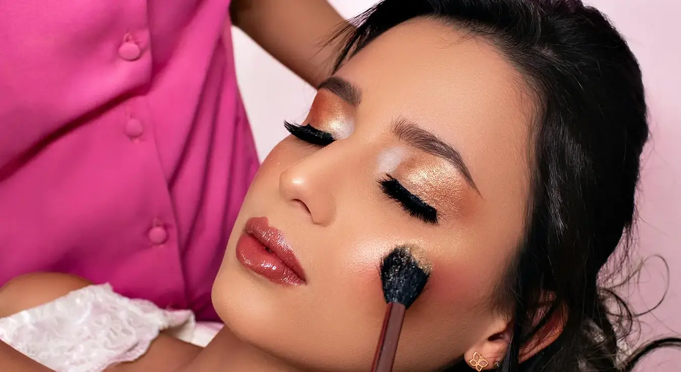 Дјевојка на столици за шминкање док је друга дјевојка шминка