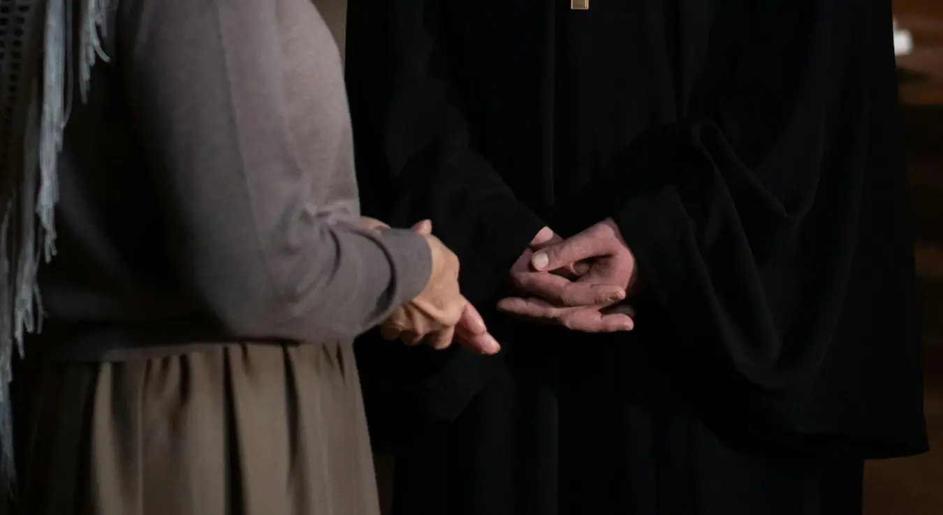 Свештеник  прекрштених руку разговара са женом у цркви-