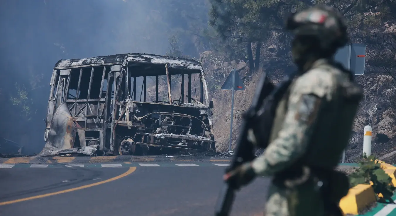 Војник стоји на стражи поред угљенисаног возила након што је запаљено, у Коинцију, држава Мичоакан, Мексико, у недјељу, 22. фебруара 2026. године, након смрти вође картела Халиско Нова генерација, Немесија Осегере, познатог као „Ел Менчо“.