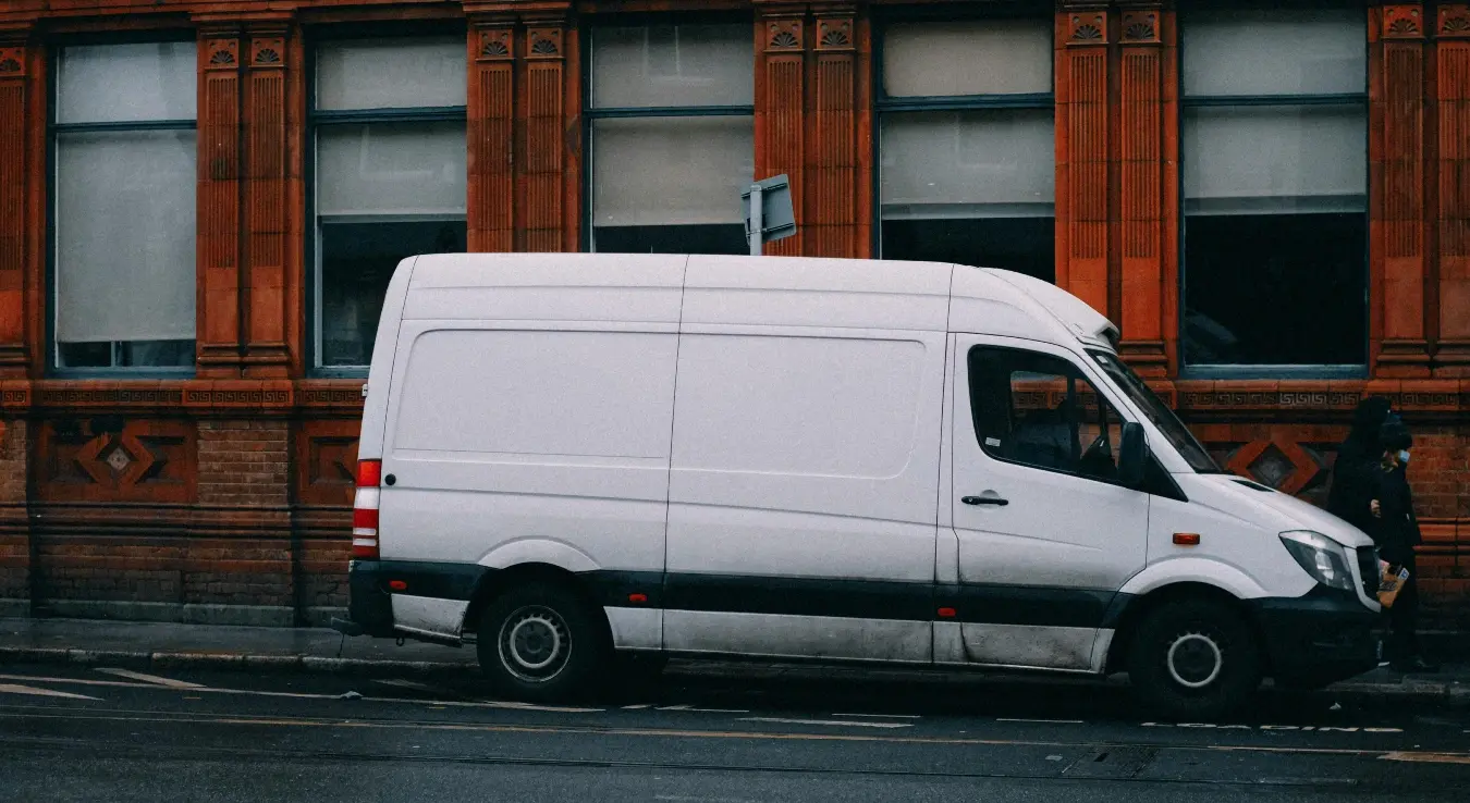 Паркиран бијели комби испред зграде.