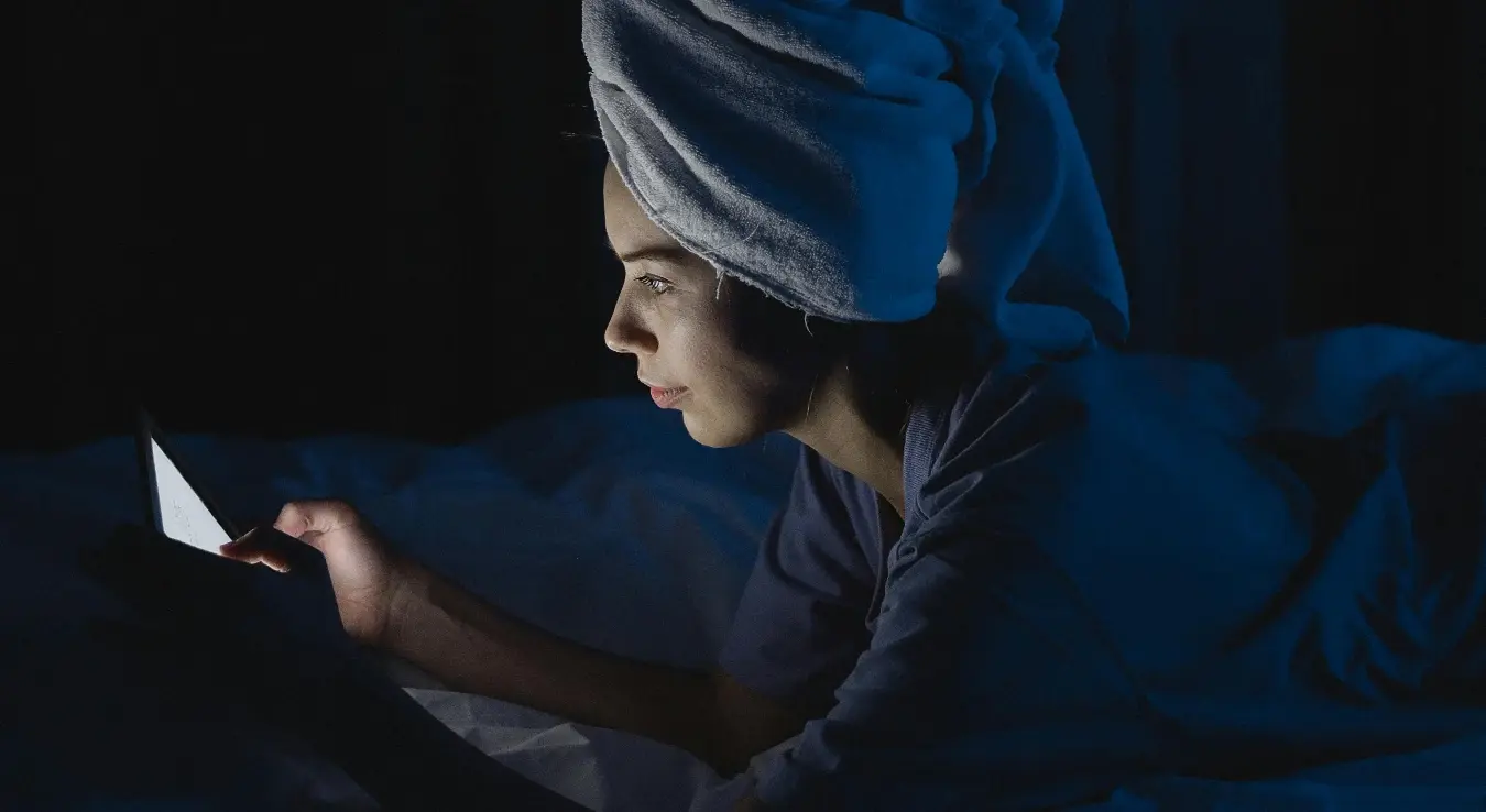 Жена лежи у кревету током ноћи и гледа у телефон