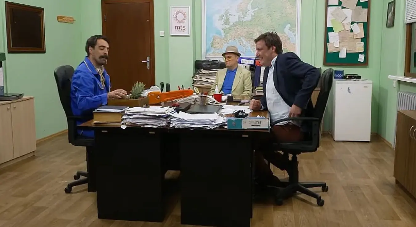 Драган Торбица, Ђорђе Чварков и Бошкић, главни ликови у серији Државни посао, сједе за столом. Инсерт из серије