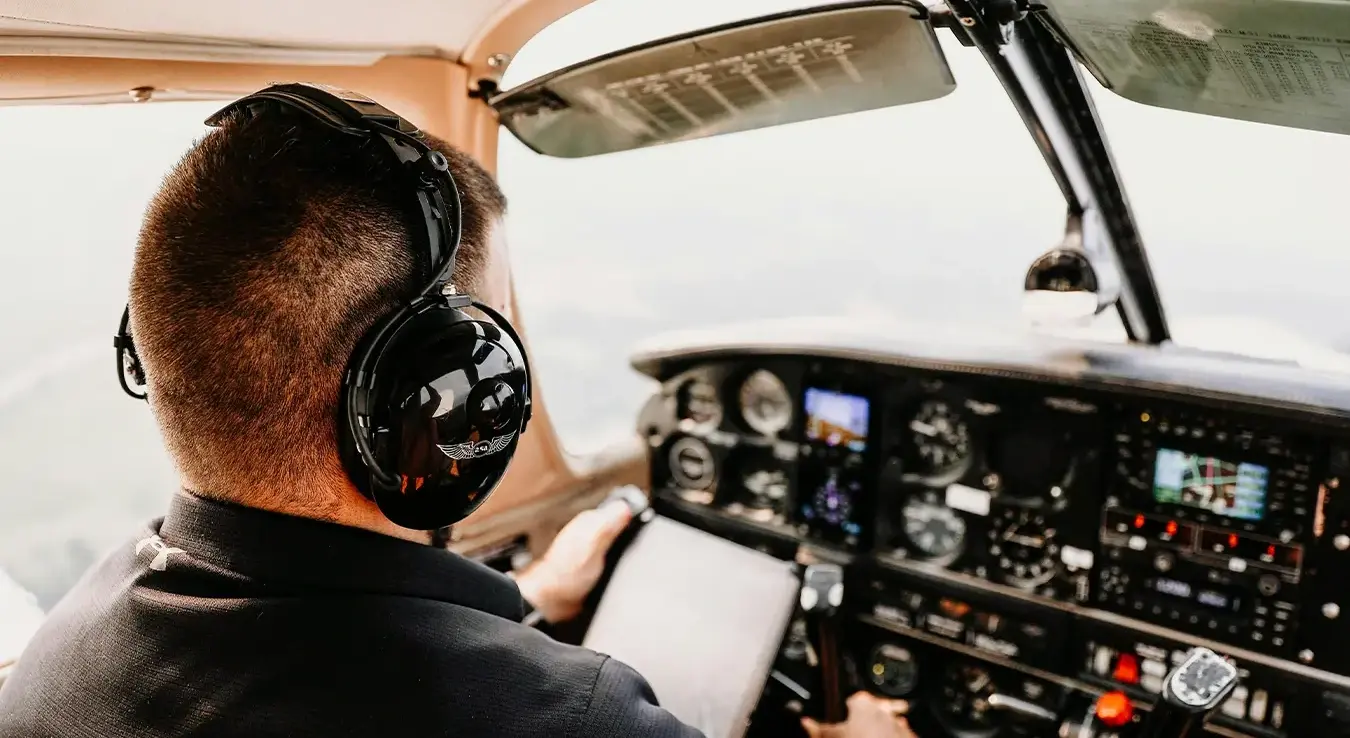 Пилот са слушалицама на ушима управља авионом.