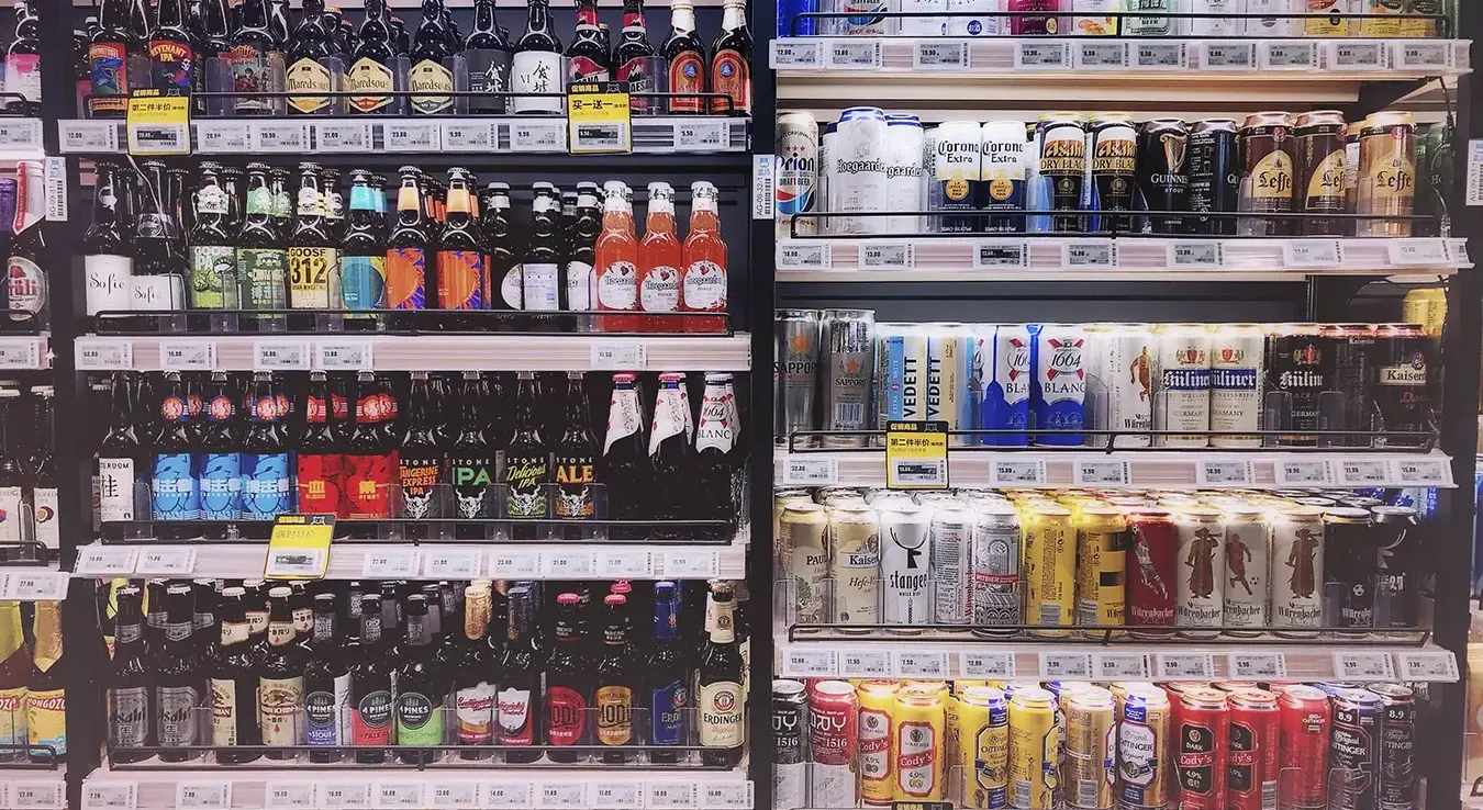 Широк избор флашираних и пива у лименкама изложен на полицама продавница.