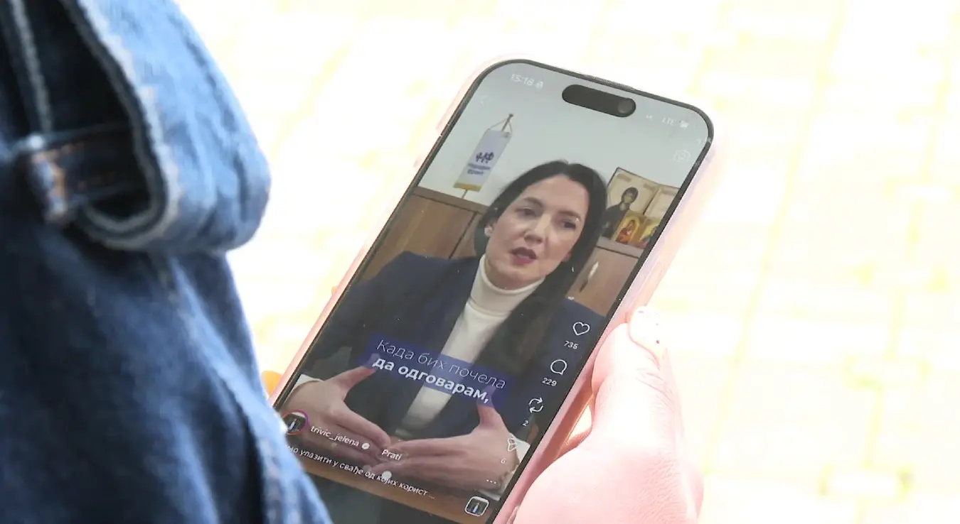 Приказана је особа која у рукама држи паметни телефон на чијем екрану се репродукује видео-снимак Јелене Тривић која говори.