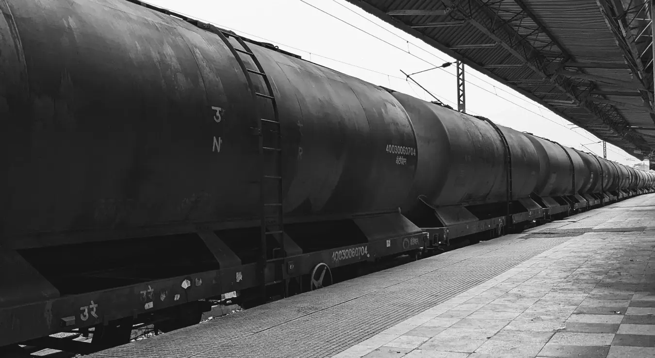 Сива слика дугог теретног воза на жељезничкој станици, која приказује индустријски транспорт.