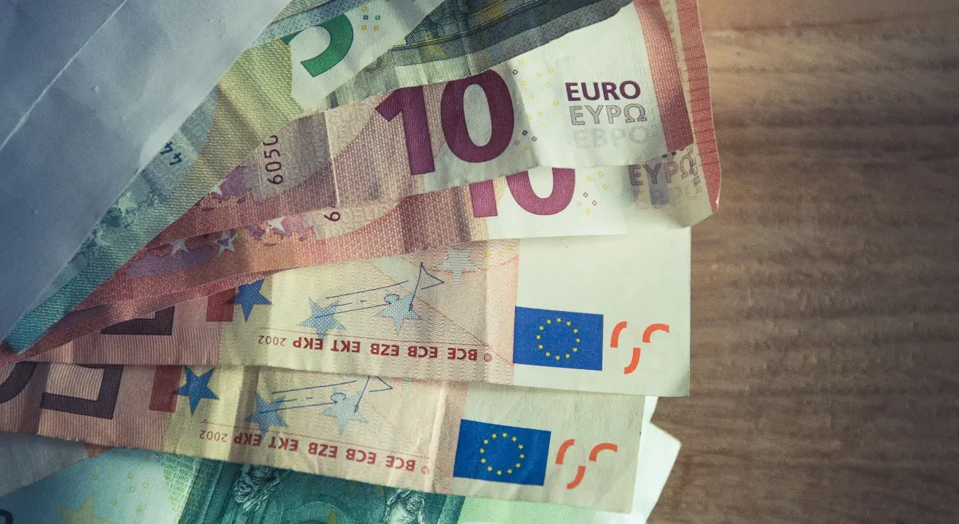 Колекција евро новчаница које излазе из коверте на дрвеној површини.